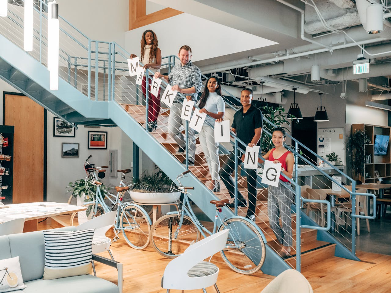 Diverse coworkers holding MARKETING signs on staircase in modern office.