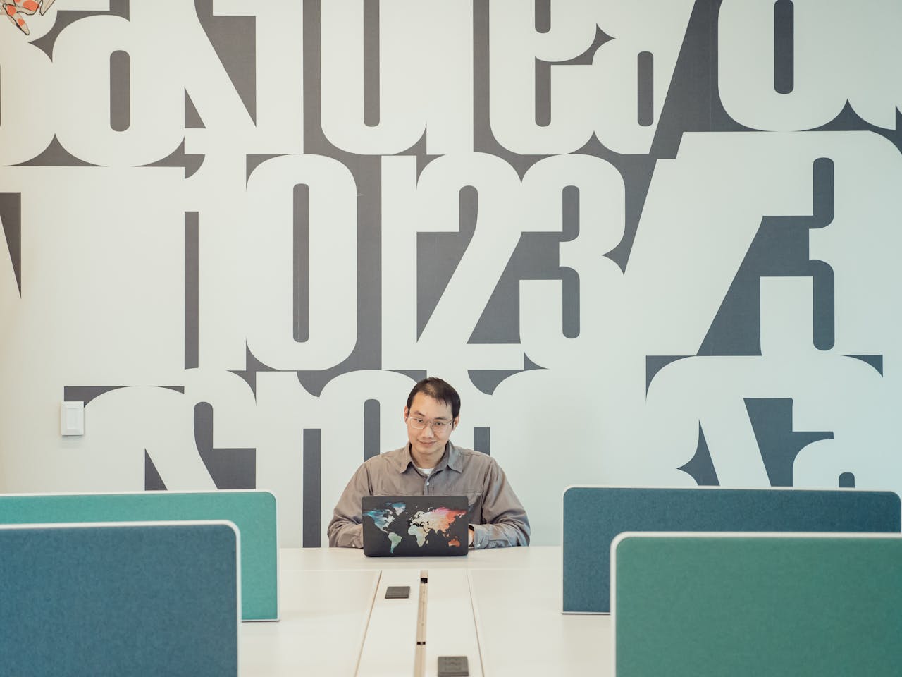 Asian man working on a laptop in a modern office with bold typography decor.